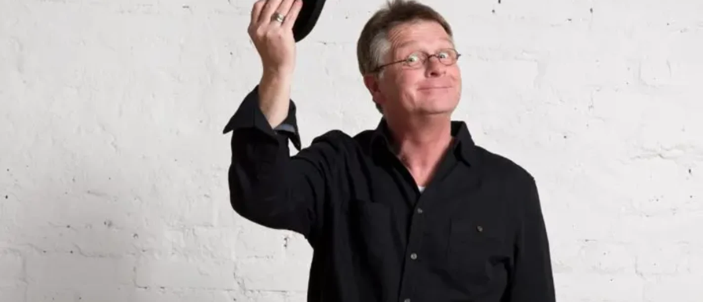 Hagen Möckel mit Brille und schwarzem Hemd hält einen schwarzen Hut vor weißer Wand.