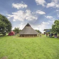 Radeln auf dem OC 3 - Rund um Venne - Mühle, Moor und Varusschlacht Rundes Reetdachhaus umgeben von grüner Wiese, Bäumen und bunten Zelten an einem sonnigen Tag.