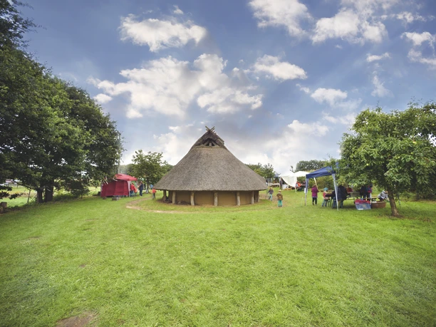Radeln auf dem OC 3 - Rund um Venne - Mühle, Moor und Varusschlacht Rundes Reetdachhaus umgeben von grüner Wiese, Bäumen und bunten Zelten an einem sonnigen Tag.