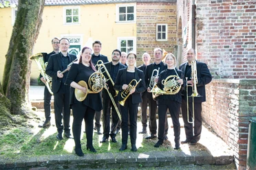 Blechbläser-Ensemble FriesenBlech mit Instrumenten vor einer Backsteinkirche.