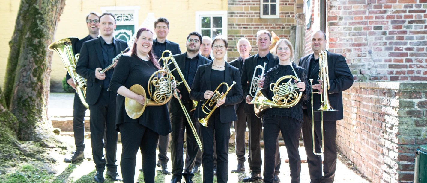 Blechbläser-Ensemble FriesenBlech mit Instrumenten vor einer Backsteinkirche.