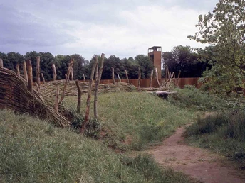 Radeln auf dem OC 3 - Rund um Venne - Mühle, Moor und Varusschlacht Holzpfähle und ein turmartiges Gebäude umgeben eine Wiese mit einem Pfad im Vordergrund.Wooden posts and a tower-like building surround a meadow with a path in the foreground.Træstolper og en tårnlignende bygning omgiver en eng med en sti i forgrunden.Houten palen en een torenachtig gebouw omringen een weiland met een pad op de voorgrond.