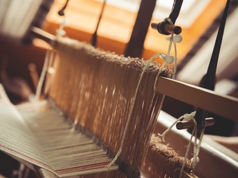 Radeln auf dem OC 1 - Rund um Ostercappeln - Wiegbold, Windthorst und Waldesruh Webstuhl mit Licht von Dachfenster, Garnfäden gespannt auf Webrahmen, Fokus auf Details der Weberei.