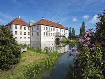 Radeln auf der NST -Tour Weißes Wasserschloss mit roten Dächern, umgeben von einem Wassergraben unter blauem Himmel.