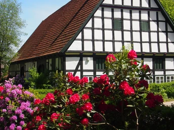 Radeln auf der BE 1 - Kleine Schlössertour Fachwerkhaus mit rotem Dach, umgeben von blühenden Rhododendren und Bäumen im Hintergrund.