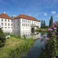 Radeln auf der BE 3 - Rund um Bad Essen Barockschloss mit rotem Dach spiegelt sich in stiller Wassergrabenlandschaft bei blauem Himmel.