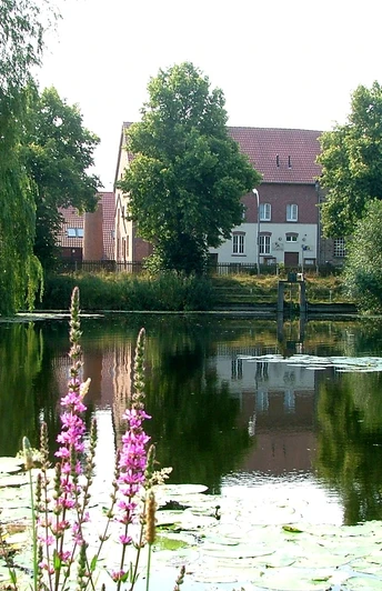 Fahrradtour "Rund um Belm" Historische Backsteingebäude spiegeln sich in einem von Seerosen bedeckten Teich.