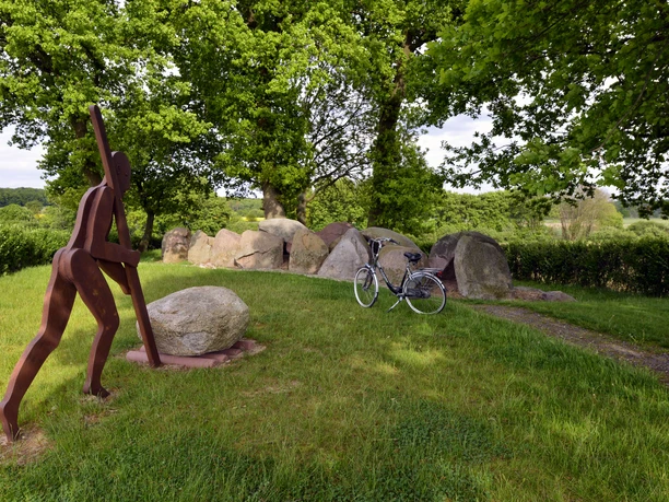 Radeln auf der Bissendorfer Rundtour Nord Beeld van een fietser naast een geparkeerde fiets op een groen grasveld, omringd door bomen.