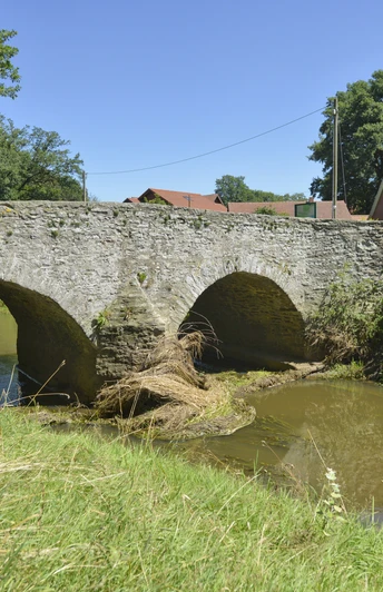 Radeln auf dem BO 2 - Rund um Hunteburg Steinbrücke mit zwei Bögen über einen Fluss, umgeben von Natur und roten Ziegeldächern.