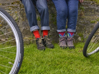 Radeln auf der Rundtour "BO 3 - Rund um Herringhausen - Stirpe - Oelingen" Zwei Personen in Jeans und bunten Socken sitzen auf einer Mauer, Fahrräder im Vordergrund.