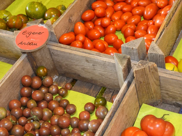Verschillende soorten tomaten in houten kratten op een markt met een bordje "Van eigen bodem".