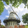 Unterwegs auf derOsning-Route Weißer Mühlenturm umgeben von blühenden Pflanzen und grünem Laub unter blauem Himmel.White mill tower surrounded by flowering plants and green foliage under a blue sky.Hvidt mølletårn omgivet af blomstrende planter og grønt løv under en blå himmel.Witte molentoren omringd door bloeiende planten en groen gebladerte onder een blauwe hemel.