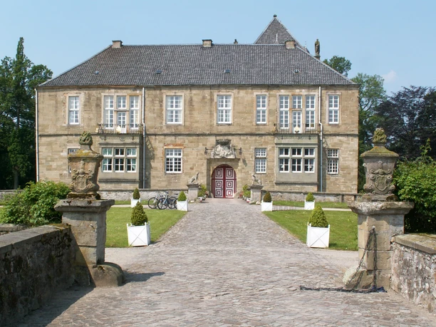 Radeln auf dem M6 - Rund um Oldendorf / Gesmold Historisches Schloss aus Sandstein mit roter Eingangstür, eingerahmt von gepflegten Büschen.