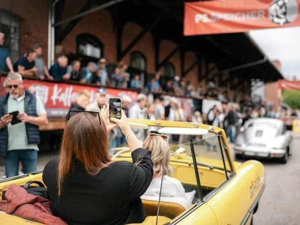 PS.SPEICHER Rallye 2026 Frau fotografiert aus gelbem Oldtimer-Cabriolet die PS.SPEICHER Rallye mit Zuschauern.