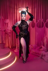 Bettie Bombshell Burlesque-Künstlerin im schwarzen Spitzenkleid posiert vor pinken Vorhängen