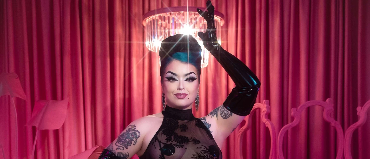 Bettie Bombshell Burlesque-Künstlerin im schwarzen Spitzenkleid posiert vor pinken Vorhängen