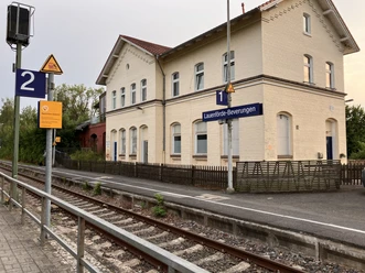 Schienen mit dem alten Bahnhofsgebäude und einem Schild Lauenförde-Beverungen