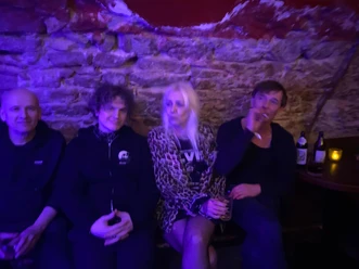 Vier Personen an einer Steinwand in blau-violettem Licht.
