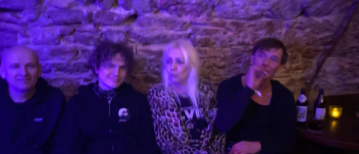 Vier Personen an einer Steinwand in blau-violettem Licht.