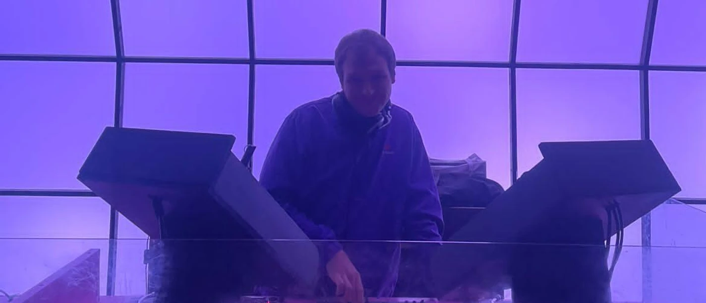 DJ an Mischpult unter violett beleuchteter Decke