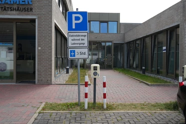 Eine E-Ladesäule an einem Parkplatz vor einem Gebäude.