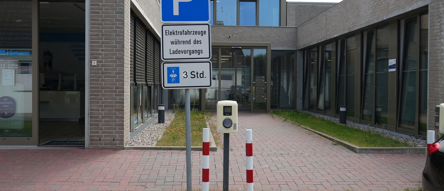 Eine E-Ladesäule an einem Parkplatz vor einem Gebäude.