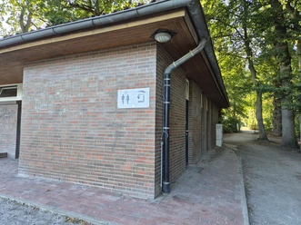 Backsteingebäude der öffentlichen Toilette am Turnierplatz, umgeben von Bäumen.