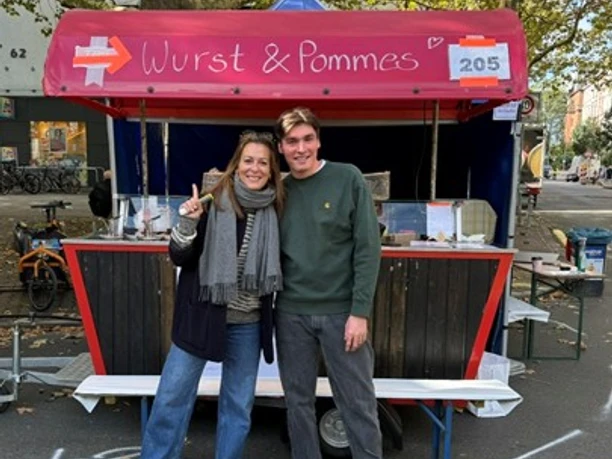 Two people in front of “Wurst & Pommes” food stall