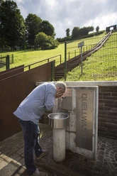 Mann erfrischt sich am Quellwasserbrunnen an der Himmelstreppe am Hennesee