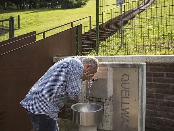 Mann erfrischt sich am Quellwasserbrunnen an der Himmelstreppe am Hennesee