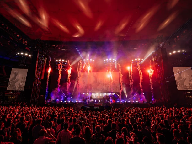 The '80s Live Audience in front of the concert stage with red lights and pyrotechnics at "Die 80er" live in Cologne