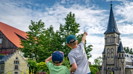 Zwei Kinder vor Miniaturgebäuden, eines zeigt auf den Kirchturm.