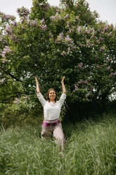 Eine Frau macht eine Yoga-Übung im hohen Gras vor einem Baum
