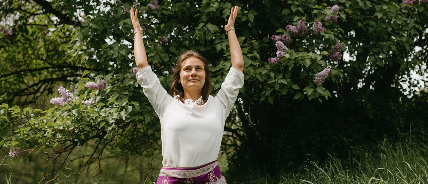 Eine Frau macht eine Yoga-Übung im hohen Gras vor einem Baum