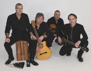 Vier Musiker in schwarzer Kleidung mit Gitarren und Cajón.