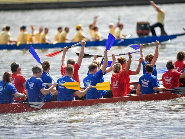 Drachenboot-Team hebt Paddel auf dem Main, weiteres Boot im Hintergrund.