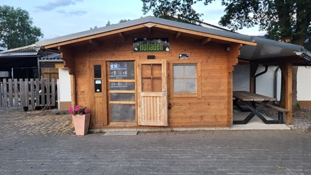 Holzhütte des Hofladens Schreiber mit Verkaufstür, Fenster und Sitzbank im Außenbereich