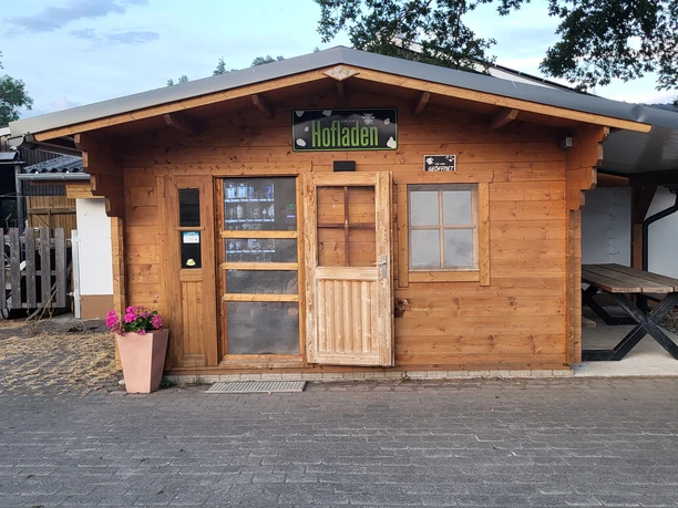 Holzhütte des Hofladens Schreiber mit Verkaufstür, Fenster und Sitzbank im Außenbereich