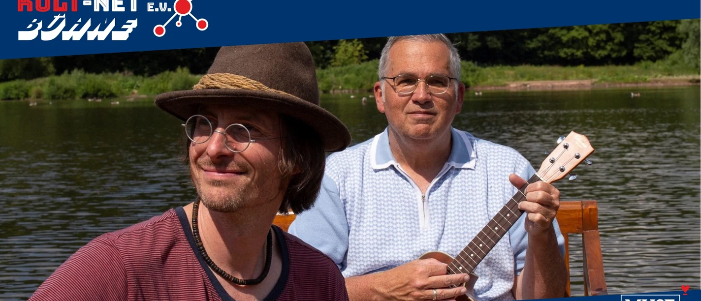 Zwei Musiker von Der Ramschladen spielen Gitarre am See.