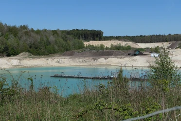 Türkisfarbener See in der Sandgrube Eggestedt mit Förderanlage und Sandhängen.