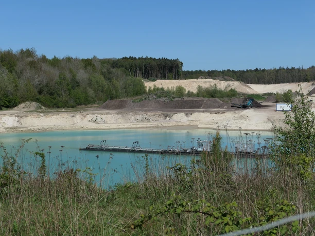 Türkisfarbener See in der Sandgrube Eggestedt mit Förderanlage und Sandhängen.