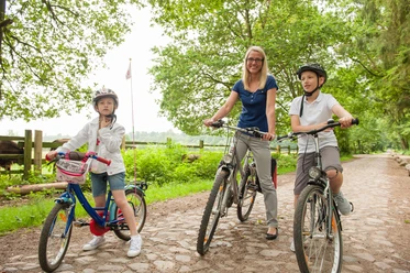 Eine Frau mit zwei Kindern und Fahrrädern unterwegs auf der Bauernhofradtour.