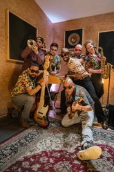 Musiker in bunten Hemden mit Instrumenten in einem Tonstudio.