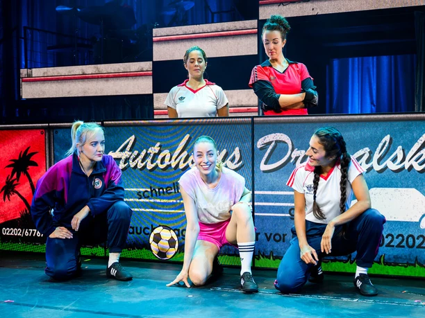 Kick Like a Woman - Ein Musical über den Mut, für Träume zu kämpfen Fünf Darstellerinnen in Fußballtrikots auf einer bunt beleuchteten Theaterbühne