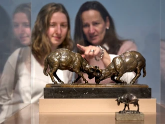 People are looking at sculptures of fighting rams in a gallery.