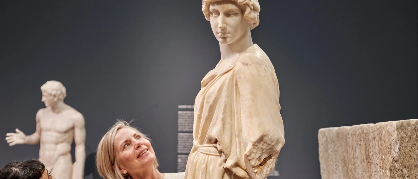 Zwei Personen betrachten eine antike Statue in einem Museum.