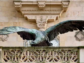 Bronzener Adler mit ausgebreiteten Flügeln auf einem verzierten Steinbalkon.