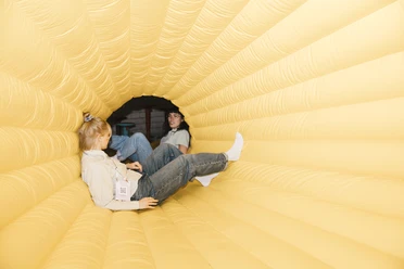 Two people are relaxing in a yellow inflatable tunnel.