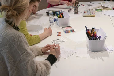 Personen zeichnen an einem Tisch mit Stiften und Papier.