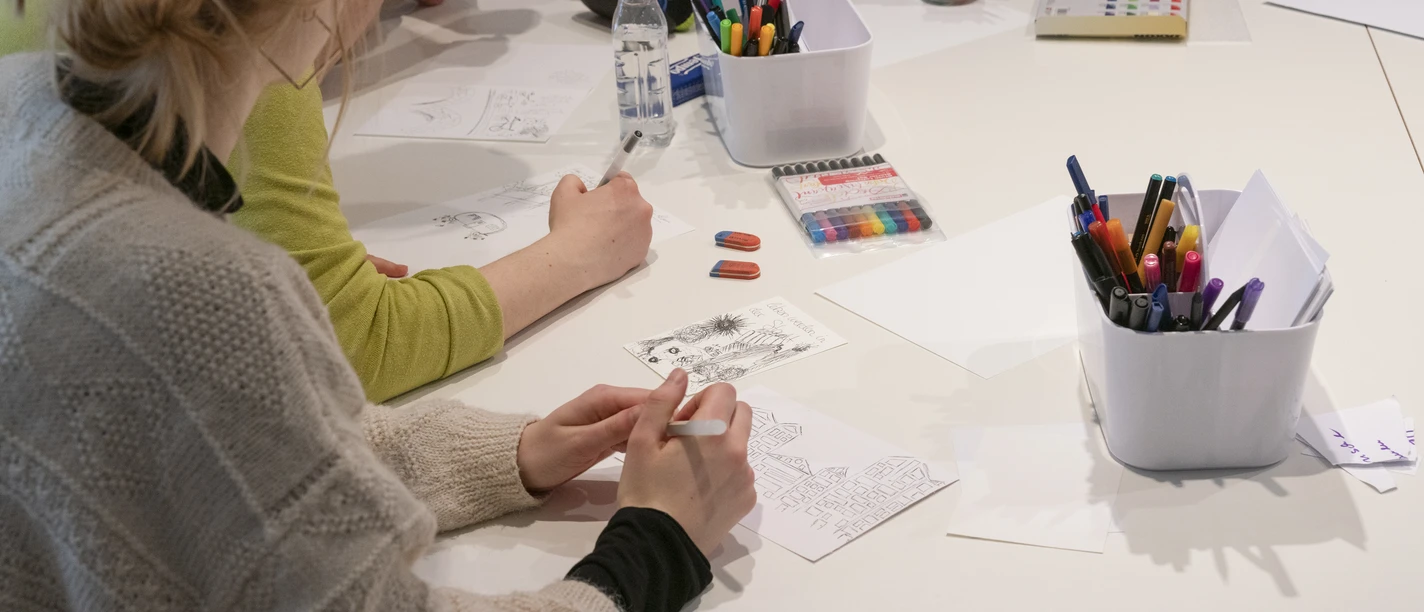 Personen zeichnen an einem Tisch mit Stiften und Papier.
